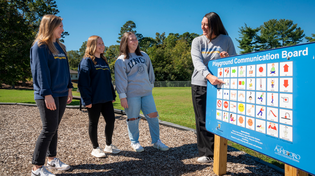 UNCG's Dr. Emily Hamuka and students look at one of their newly implemented playground communication boards